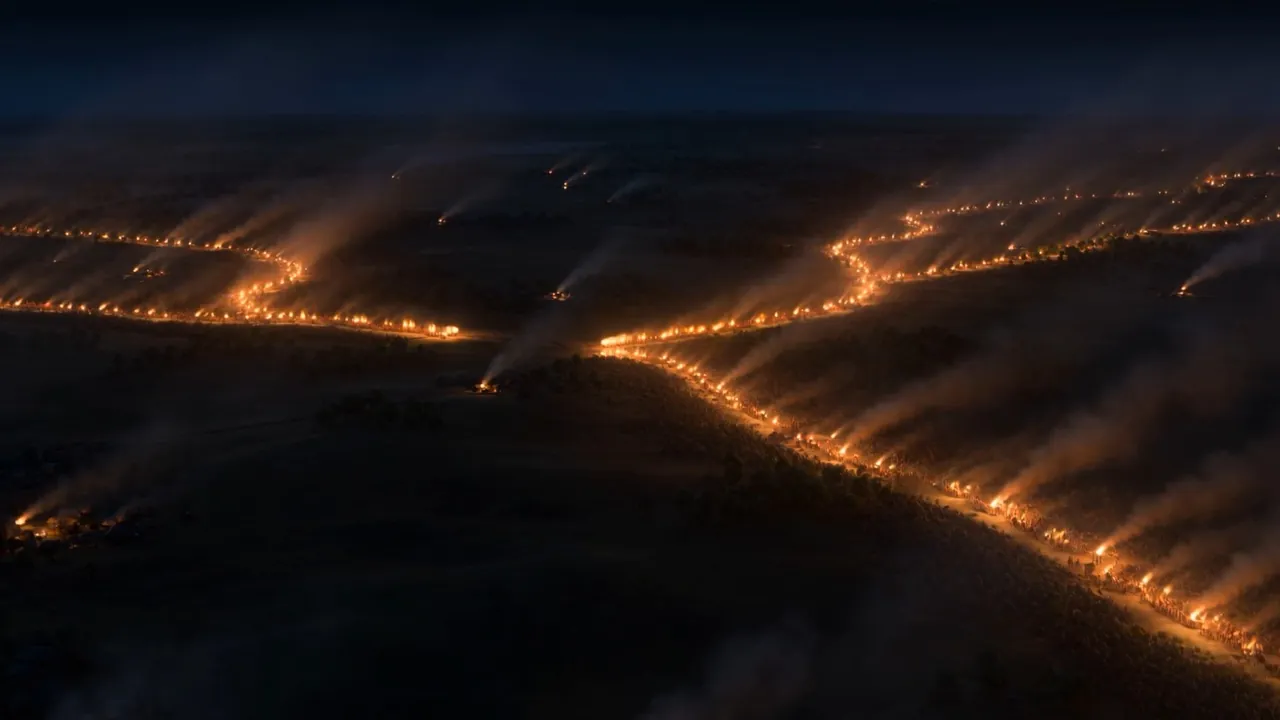 Two rivers of torchlight flow toward one another in the dark